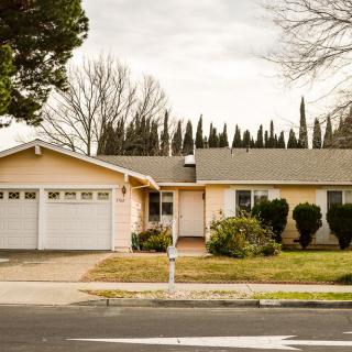 A suburban house with a front yard and attached garage, set against a backdrop of tall trees.
