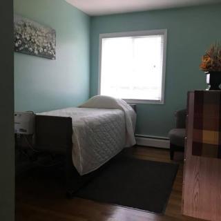 A cozy, minimalist bedroom with a single bed and green walls, lit by natural light from a window.