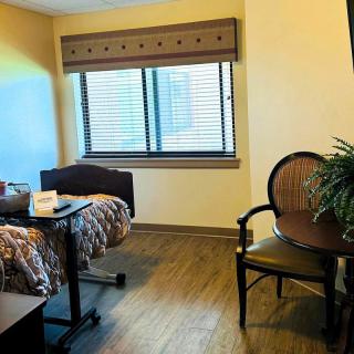 A tidy hospital room with a bed near the window, a small table with chairs, and a lamp on the nightstand.