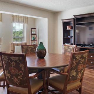 A cozy dining area with a wooden table and floral chairs, adjacent to a living room space with an entertainment center.
