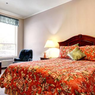 A cozy hotel room featuring a bed with floral bedding, a lamp, and a chair by the window.