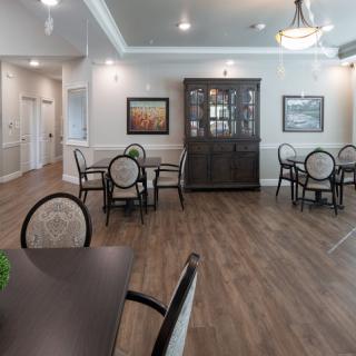 A spacious dining area featuring round tables, chairs, a cabinet, and soft lighting.