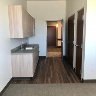 A narrow office hallway with a sink and cabinets, featuring wood flooring and multiple doors.