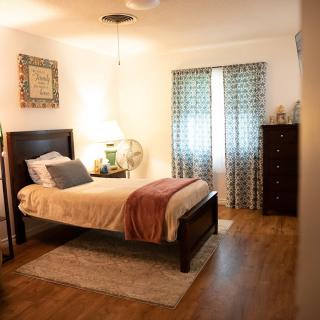 A cozy bedroom with a neatly made bed, a lamp on a nightstand, and patterned curtains.