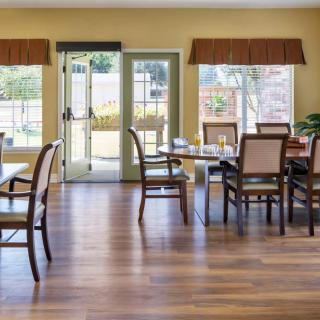 A well-lit dining room with several tables and chairs arranged on a wooden floor.