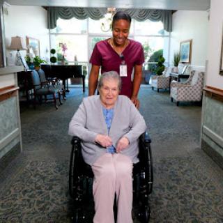 A caregiver assists an elderly woman in a wheelchair at a healthcare facility.