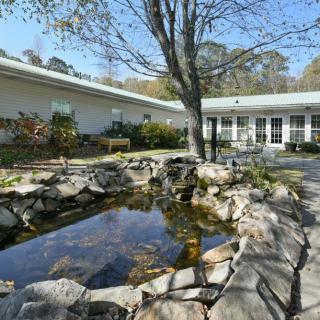 A tranquil garden setting with a pond surrounded by rocks and trees, adjacent to a building.