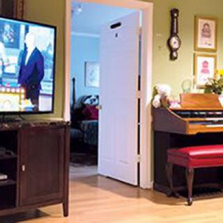 A cozy living room featuring a television, an organ with a red bench, and wooden flooring.