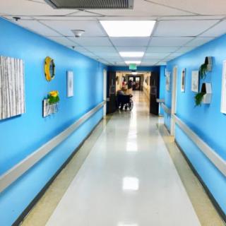 A brightly lit hospital corridor with blue walls and artwork.