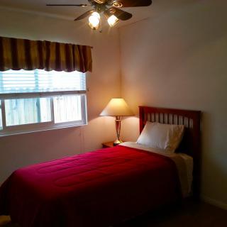 A cozy bedroom with a single bed and red bedding, illuminated by a lamp next to the window.