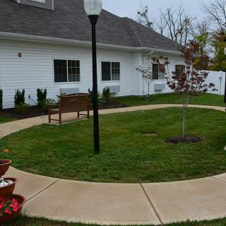 A circular garden path with a bench and lamp post surrounded by a well-maintained lawn and small trees in front of a building.