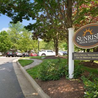 Entrance to Sunrise Senior Living community with surrounding trees and parking lot.