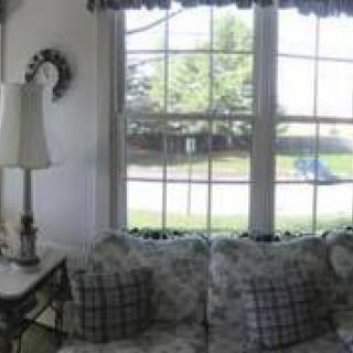 A cozy living room with a large window and floral sofa adorned with plaid cushions.