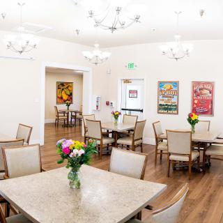 A well-lit dining area with several tables and chairs, decorated with flowers and artwork on the walls.