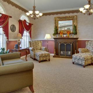 A traditional living room with elegant decor featuring a fireplace, armchairs, chandeliers, and draped windows.