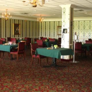 An empty restaurant dining room with neatly arranged tables and chairs, complemented by chandeliers and patterned wallpaper.
