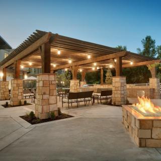 An inviting outdoor patio with a pergola, warm lighting, and a cozy fire pit.