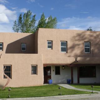 A stucco house with trees and a grassy lawn under a clear sky.