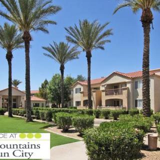 A well-maintained apartment complex with palm trees and manicured landscaping under a clear blue sky.