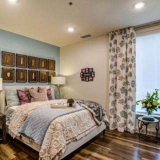 A modern and cozy bedroom with stylish decor, featuring a comfortable bed, artfully arranged pillows, wooden flooring, and decorative curtains.