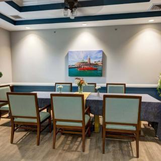 A modern dining room with a long table, multiple chairs, and artwork on the wall.