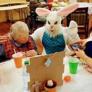 An Easter Bunny entertains an elderly person at a festive indoor event.