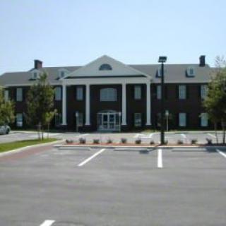 A brick building with columns and a large parking lot in front.