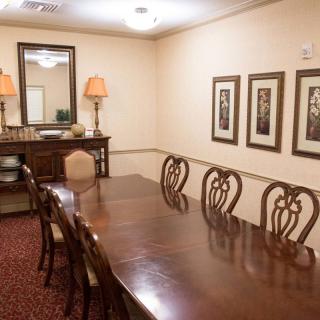 A traditional dining room with a long wooden table and elegant chairs, complemented by framed artwork and lamps.