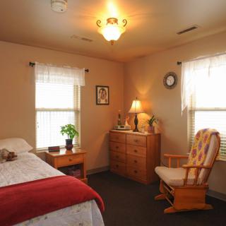 A cozy bedroom with a rocking chair, dresser, and a warmly lit lamp.