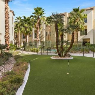 A landscaped outdoor area with palm trees and a putting green surrounded by apartment buildings.