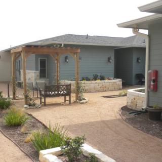 A serene outdoor setting with a house, garden pathway, and a pergola with a bench.