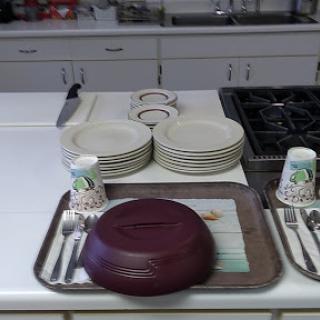 A neatly arranged kitchen counter with plates, cups, utensils, and a serving bowl.