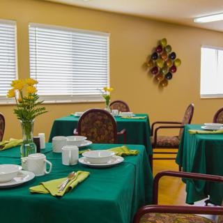 A cozy dining room with green tablecloths and neatly set tables.