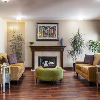 A cozy living room with a fireplace, featuring comfortable sofas, artwork on the wall, and lush green plants.