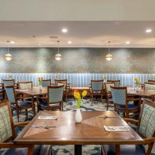 A well-lit restaurant dining area featuring neatly arranged tables and chairs, each decorated with a vase of yellow flowers.