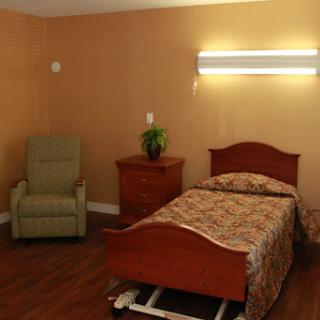 A cozy bedroom featuring a bed, a green chair, and a small nightstand with a plant.