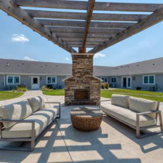 A cozy outdoor patio with a pergola, featuring comfortable seating and a stone fireplace.