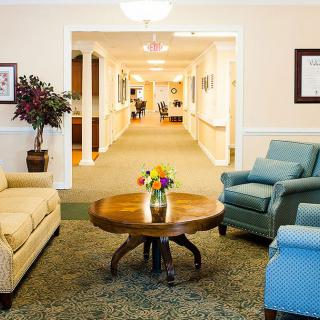 A cozy lobby area with comfortable seating and a central table adorned with flowers, leading to a well-lit hallway.