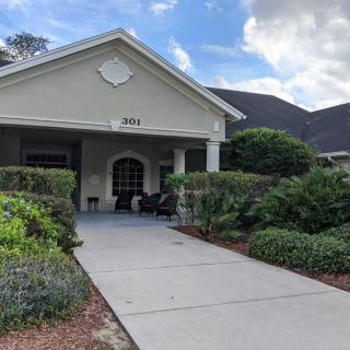A residential house with a landscaped front yard and a porch under a cloudy sky.