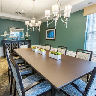 A modern dining or conference room with a large table and chairs, decorated in a contemporary style with green walls and elegant lighting.
