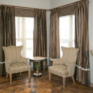 A cozy corner with two armchairs and a small table beside large windows with curtains.