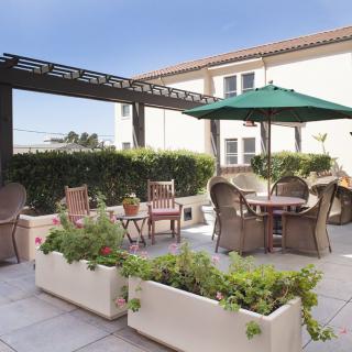 A cozy outdoor patio featuring wicker chairs, tables with umbrellas, and decorative planters on a sunny day.