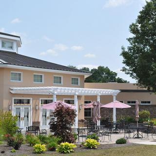A patio area with pink umbrellas, surrounded by landscaped gardens and a building in the background.