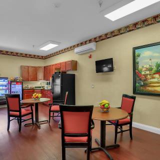 A cozy kitchenette with tables and chairs, featuring a fridge, television, and a decorative painting.