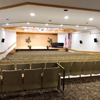 A spacious auditorium featuring seating arrangements, a stage, and decorative elements.