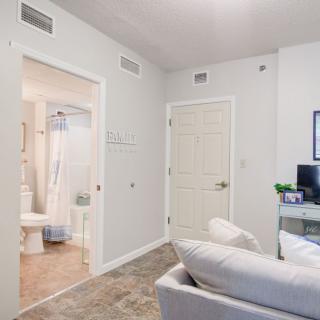 A modern, minimalist living space with a view into the bathroom, featuring bright lighting and a computer desk.