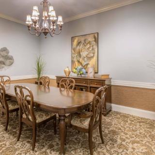 A traditional dining room featuring a wooden dining table and chairs, illuminated by a chandelier, with artwork and decorative elements adding sophistication to the space.