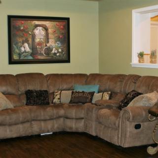 A cozy living room with a large sectional sofa, adorned with various cushions, and a framed artwork on the wall.