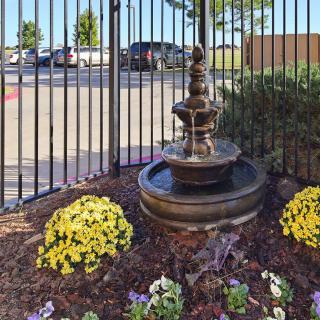 A decorative garden fountain surrounded by colorful flowers near an iron fence.