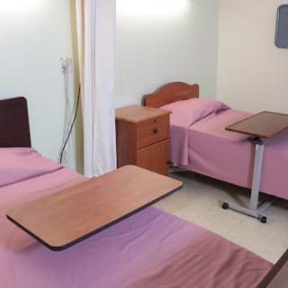 A view of a patient room in a hospital, featuring two twin beds with pink bedding and bedside furniture.